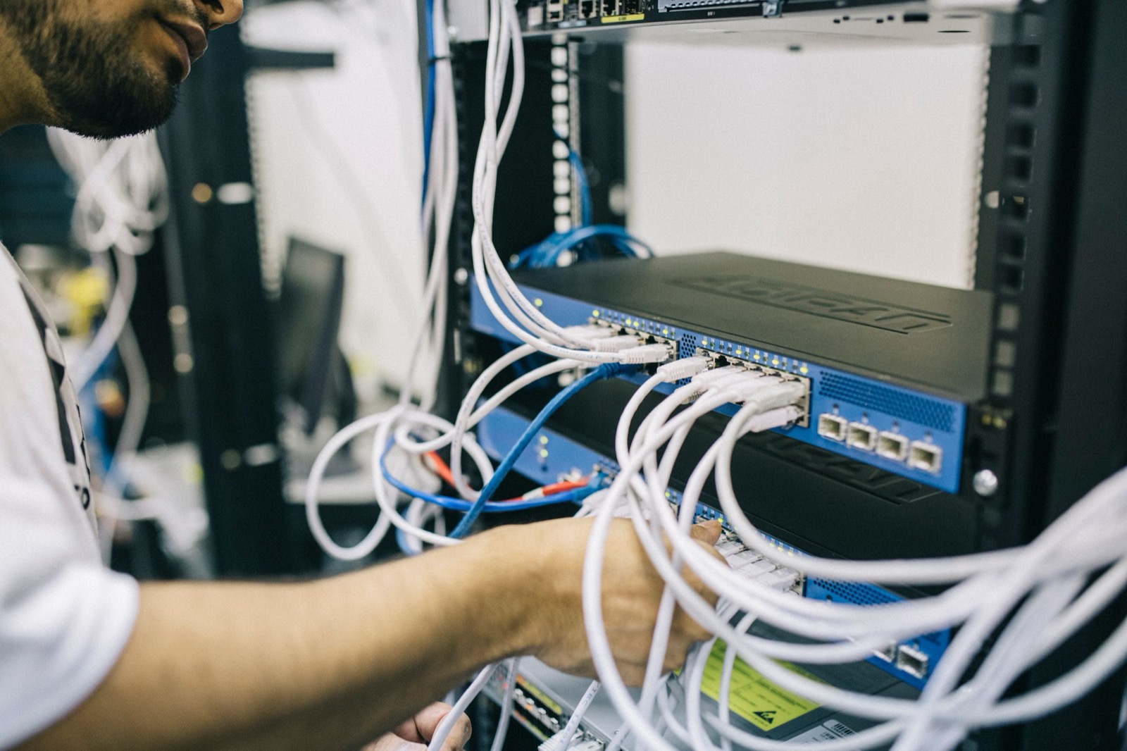 Tehnician conectând cabluri de rețea într-un rack de comunicații